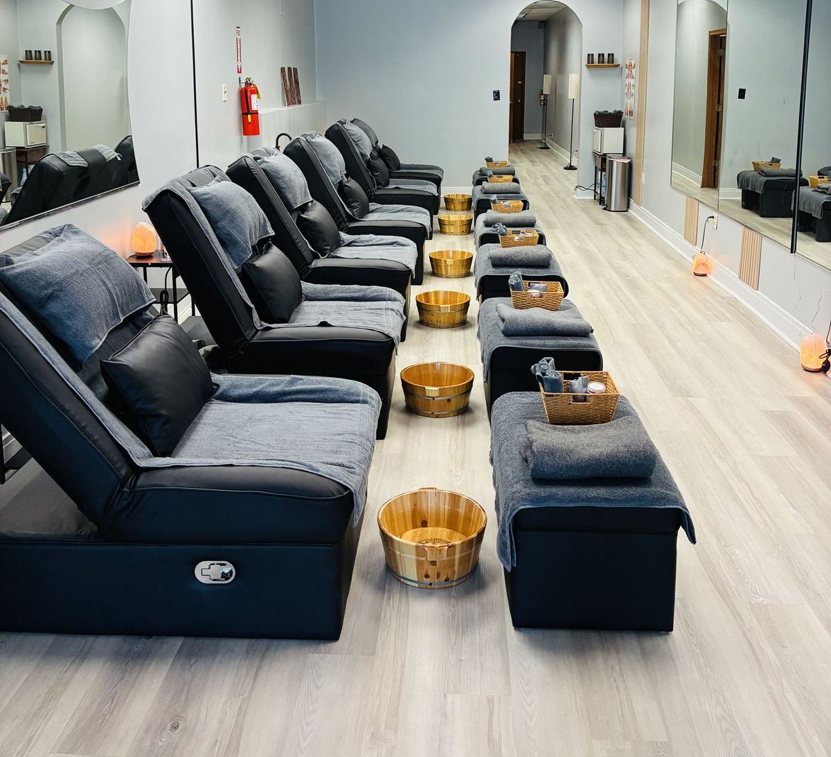 The reflexology lounge: black recliners with grey towels, wooden foot basins and pale oak floors.